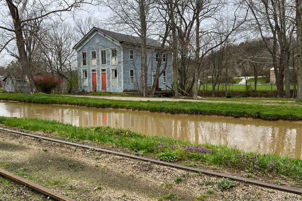 blue duplex sits on one side of a canal and a railroad runs on the other
