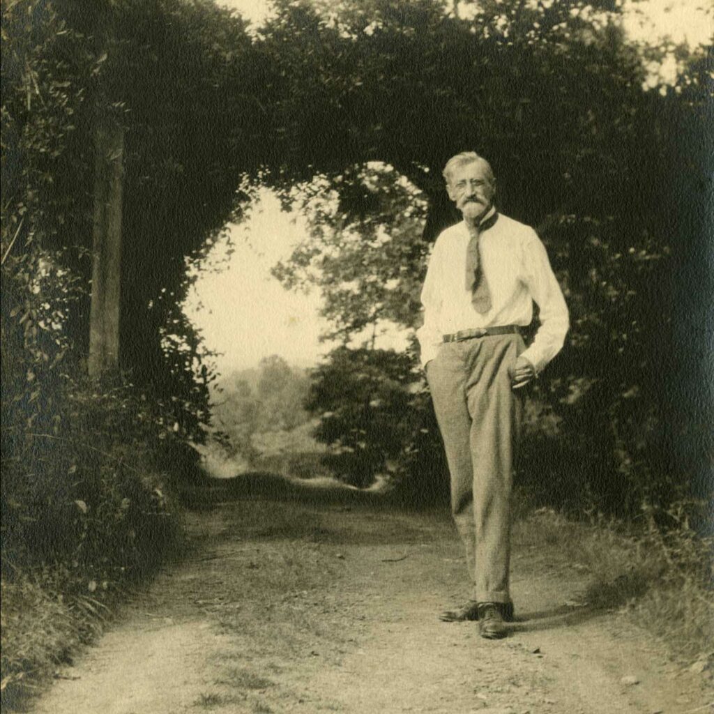 T.C. Steele stands on a dirt road framed by trees with his hands in his pockets