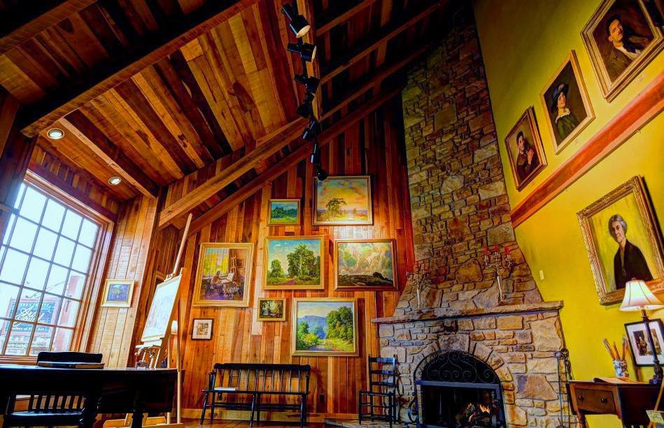a room with high ceilings, a stone fireplace, and many paintings adorning the wood panel walls
