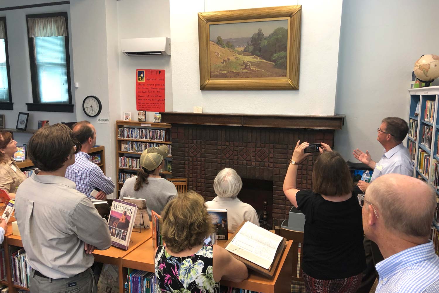 The Friends of T.C. Steele stand around the painting "In Harvest Time" discussing and taking photographs